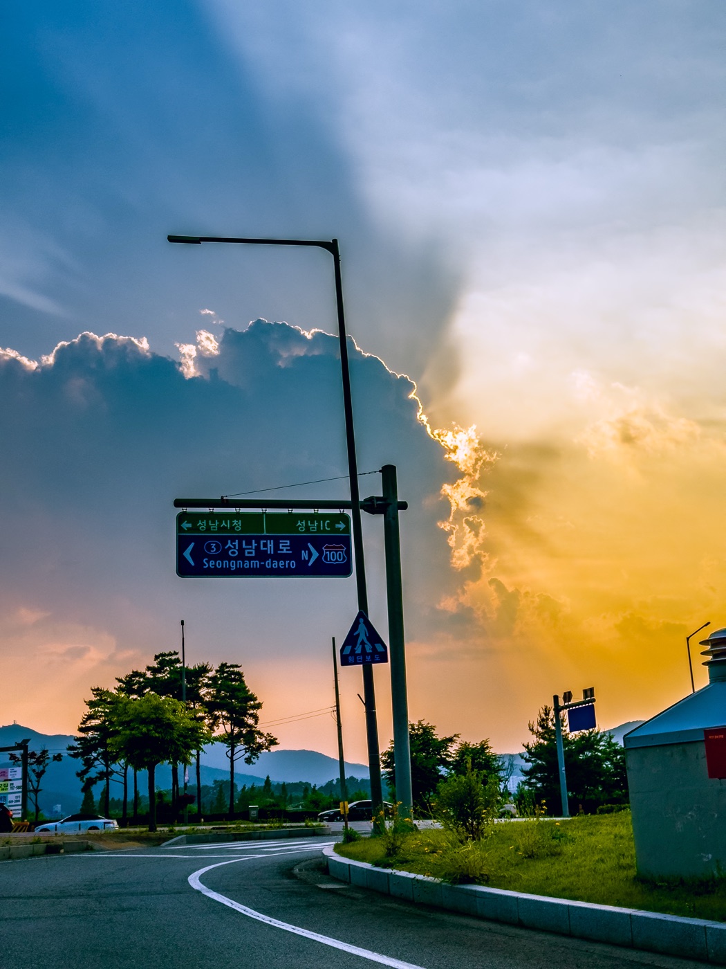 A storm clearing over a Seongnam-daero road sign at sunset, the last of the clouds lit gold against a cooling blue sky.