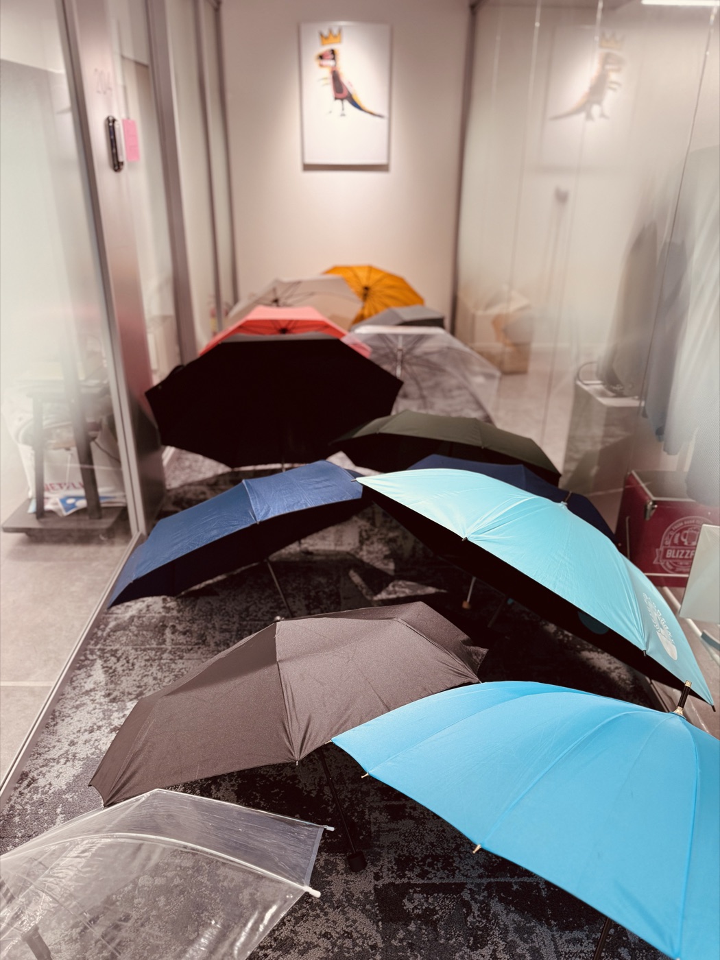 A row of drying umbrellas of every color lined up along a wet tile floor just inside a building entrance.